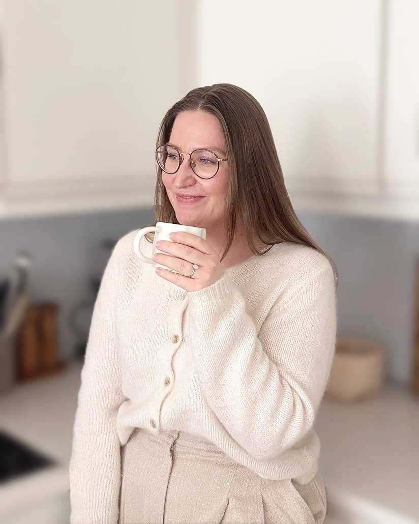Martine lener seg mot kjøkkenbenken med en kopp og smiler